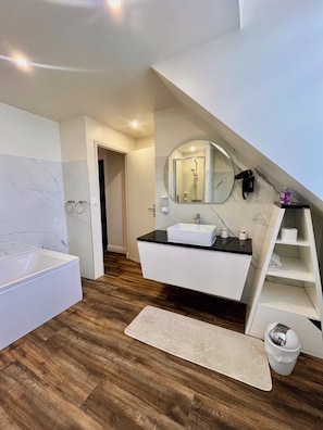 A modern bathroom with a bathtub, a vanity with a sink, a mirror, and a shower.