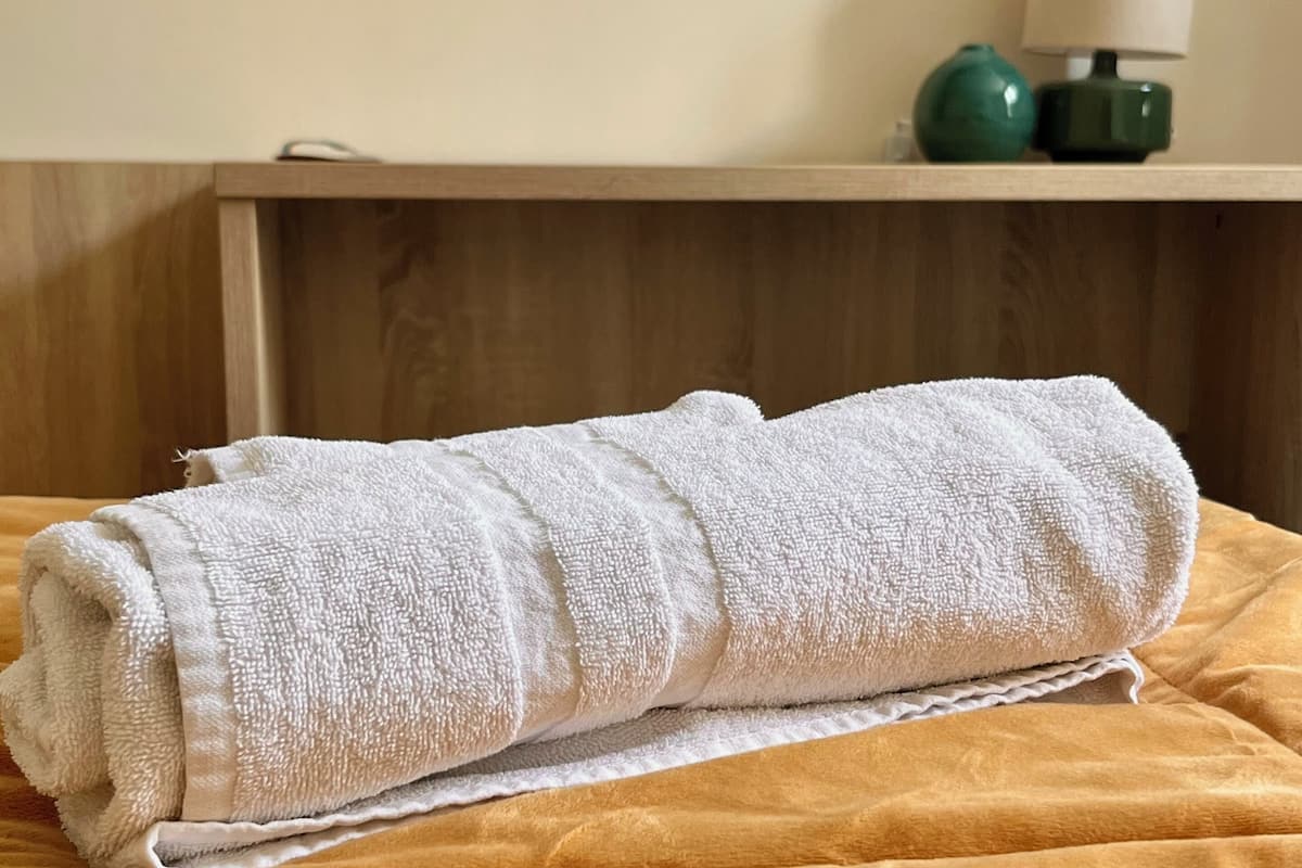 A neatly folded white towel on a bed with a yellow and green blanket.
