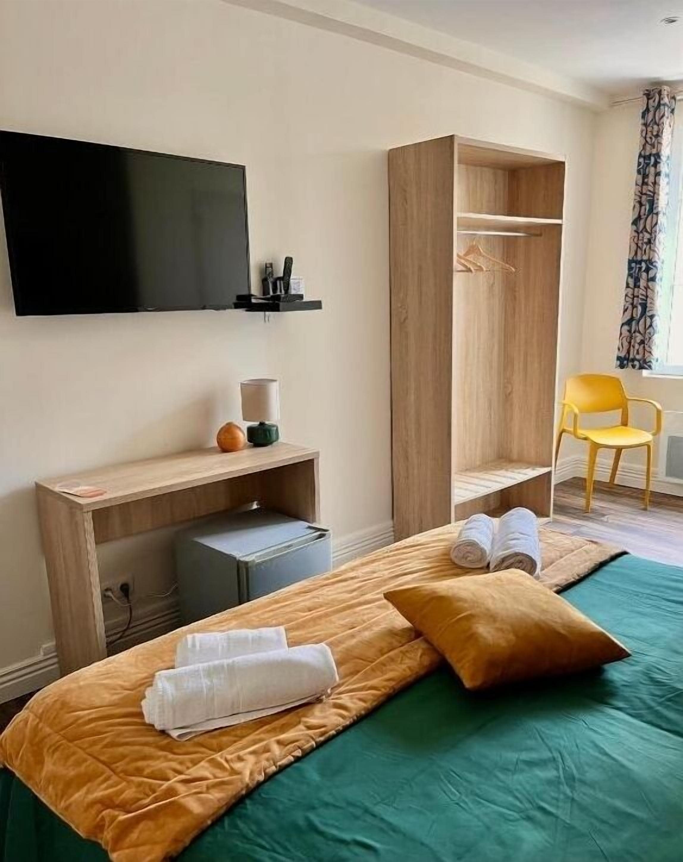 Una camera d'albergo con un letto, una scrivania con una sedia, un armadio, una TV e una finestra con tende.