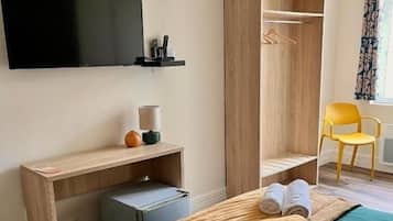 Una camera d'albergo con un letto, una scrivania con una sedia, un armadio, una TV e una finestra con tende.