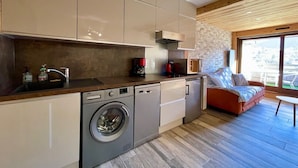 A compact kitchen with a washing machine, a coffee maker, and a sofa in a living area with a view. - Beautiful studio with magnificent view (Briançon)