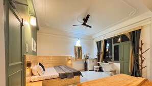 Habitación de hotel con cama, escritorio, espejo, ventilador de techo y ventana con cortinas.