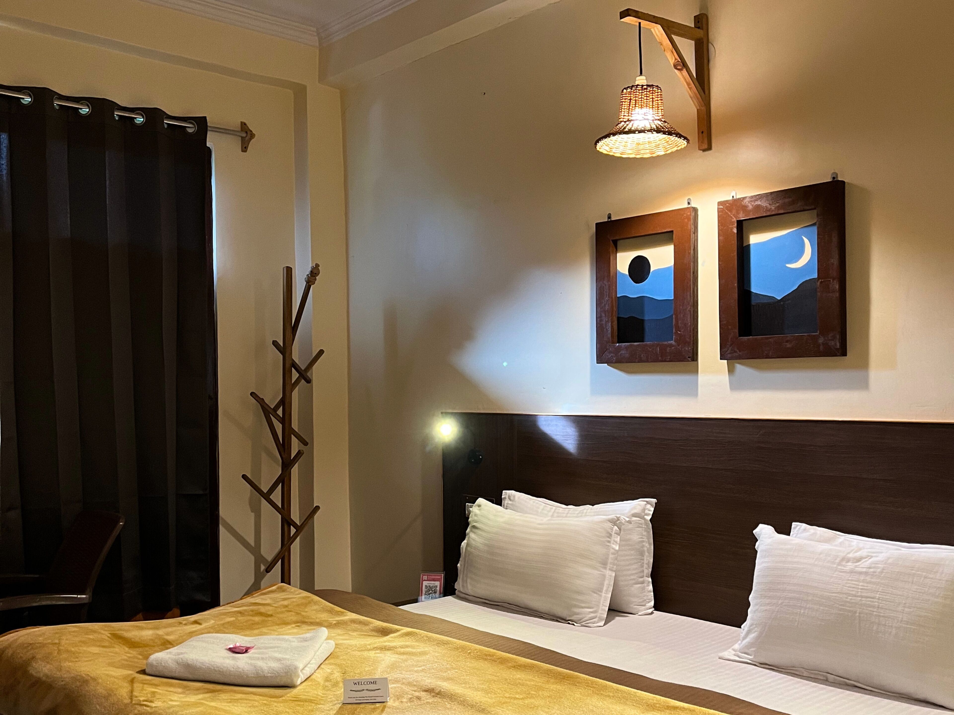 A hotel room with a bed, two wall-mounted nightlights, and a wooden coat rack.