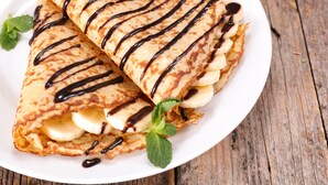 Un plato de crepas con salsa de chocolate y rodajas de plátano.