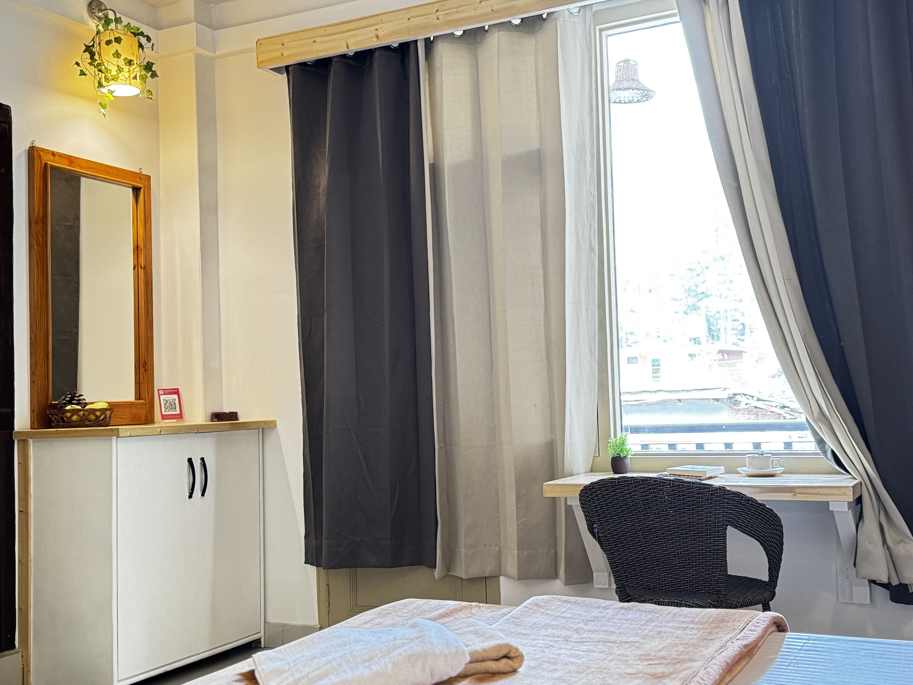 Un dormitorio con cama, ventana con cortinas, una silla, un escritorio y un espejo.