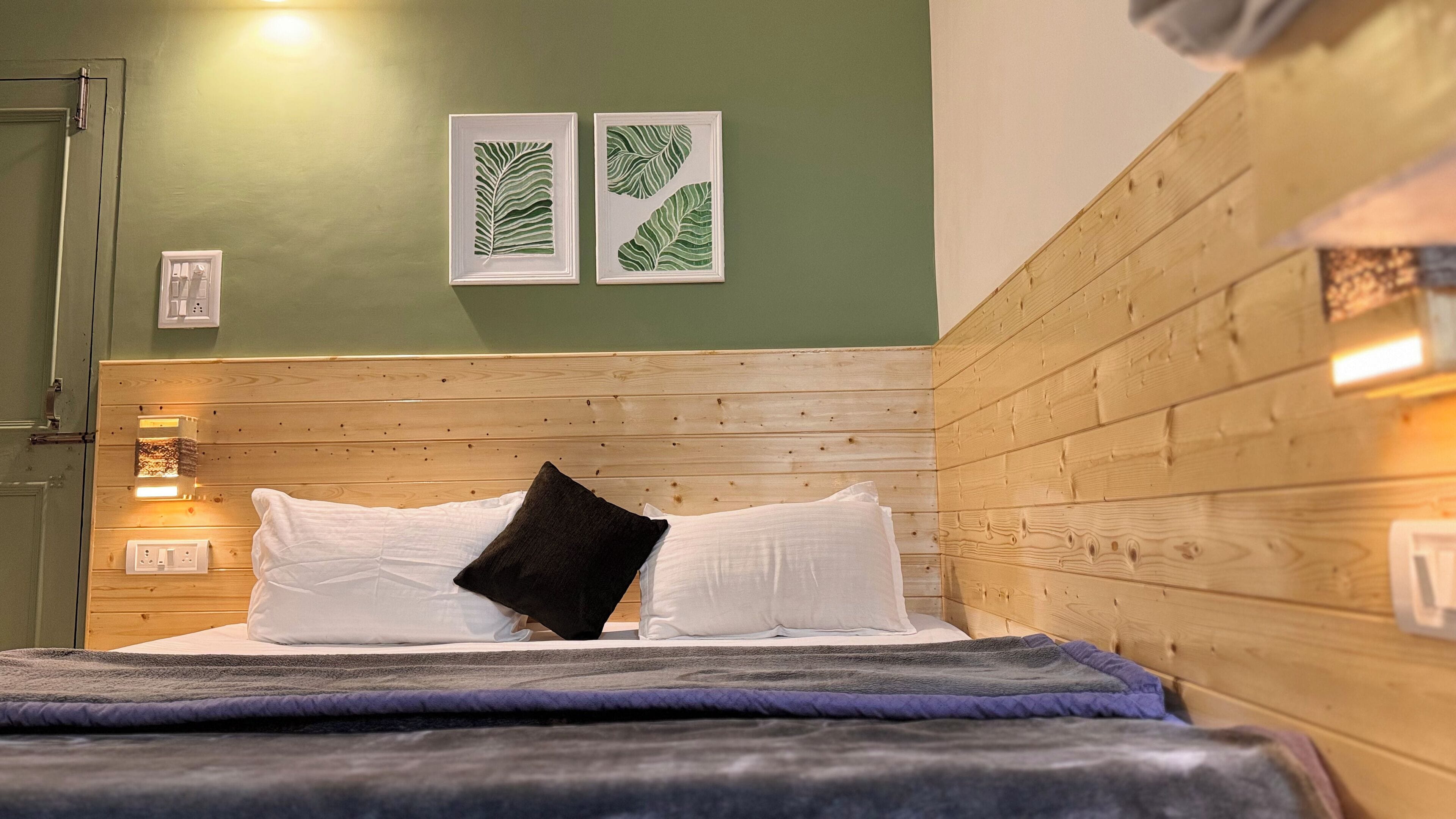 A neatly made bed with white and black pillows, a blue blanket, and a wooden headboard. There are two framed leaf artworks on the wall above the bed.