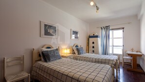 Une chambre avec deux lits, une chaise, un bureau et une fenêtre avec des rideaux.