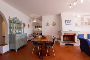 A dining area with a wooden table and chairs, a decorative cabinet, and a fireplace. - Solazur by Acasadascasas (Mafra)