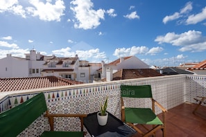 A rooftop terrace with a potted plant, two green chairs, and a tiled wall with a geometric pattern. - Solazur by Acasadascasas (Mafra)