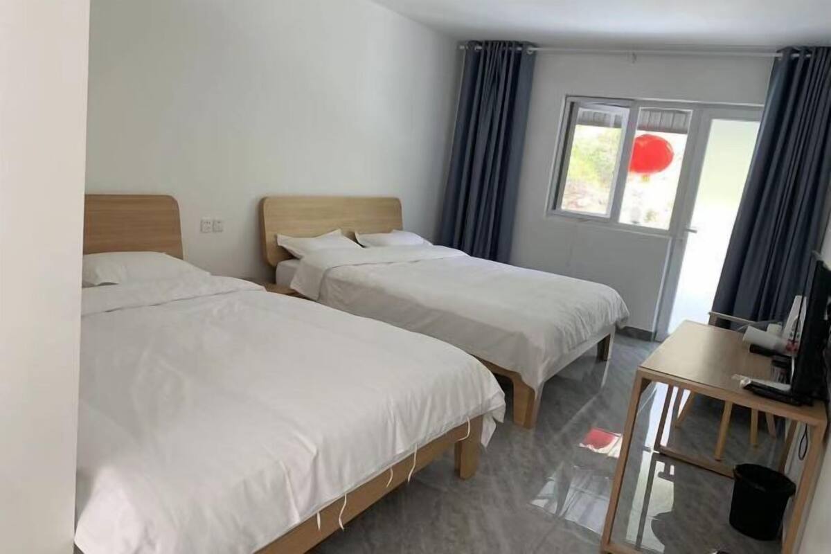 A hotel room with two single beds, a small table, and a window with curtains.