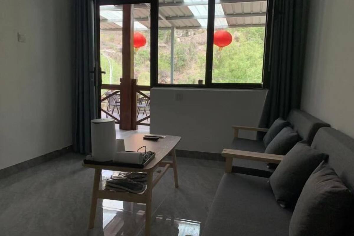 A modern room with a grey sofa, a small table with a laptop, and a window with curtains.