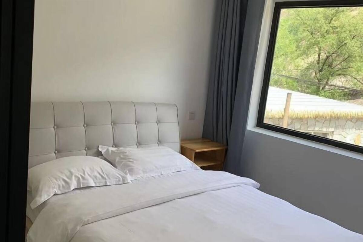 A neatly made bed with white linens, a tufted headboard, and a small wooden nightstand beside it.