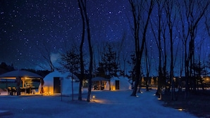 A yurt-style accommodation with a covered outdoor seating area, surrounded by trees under a starry night sky. - NAGOMI CAMP (Nasushiobara)
