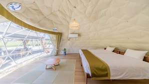 A spacious tent-style room with a large bed, a small table, and a hanging light fixture. - NAGOMI CAMP (Nasushiobara)