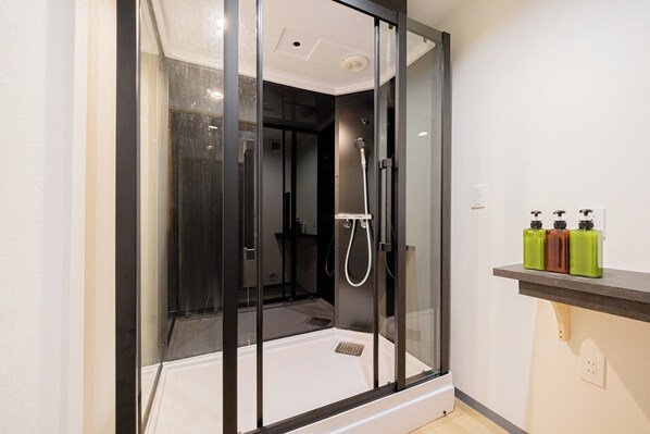 Un baño moderno con ducha envuelta en vidrio, lavamanos blanco y repisa con artículos de aseo.