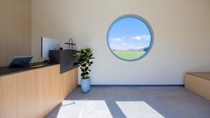 A modern reception area with a desk, laptop, and potted plant. A large window offers a view of a green field and a clear sky. - NAGOMI CAMP (Nasushiobara)