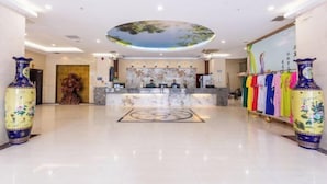 A hotel lobby with a reception desk, a large mural, and traditional vases. - Lotto Hotel (Dongxing)