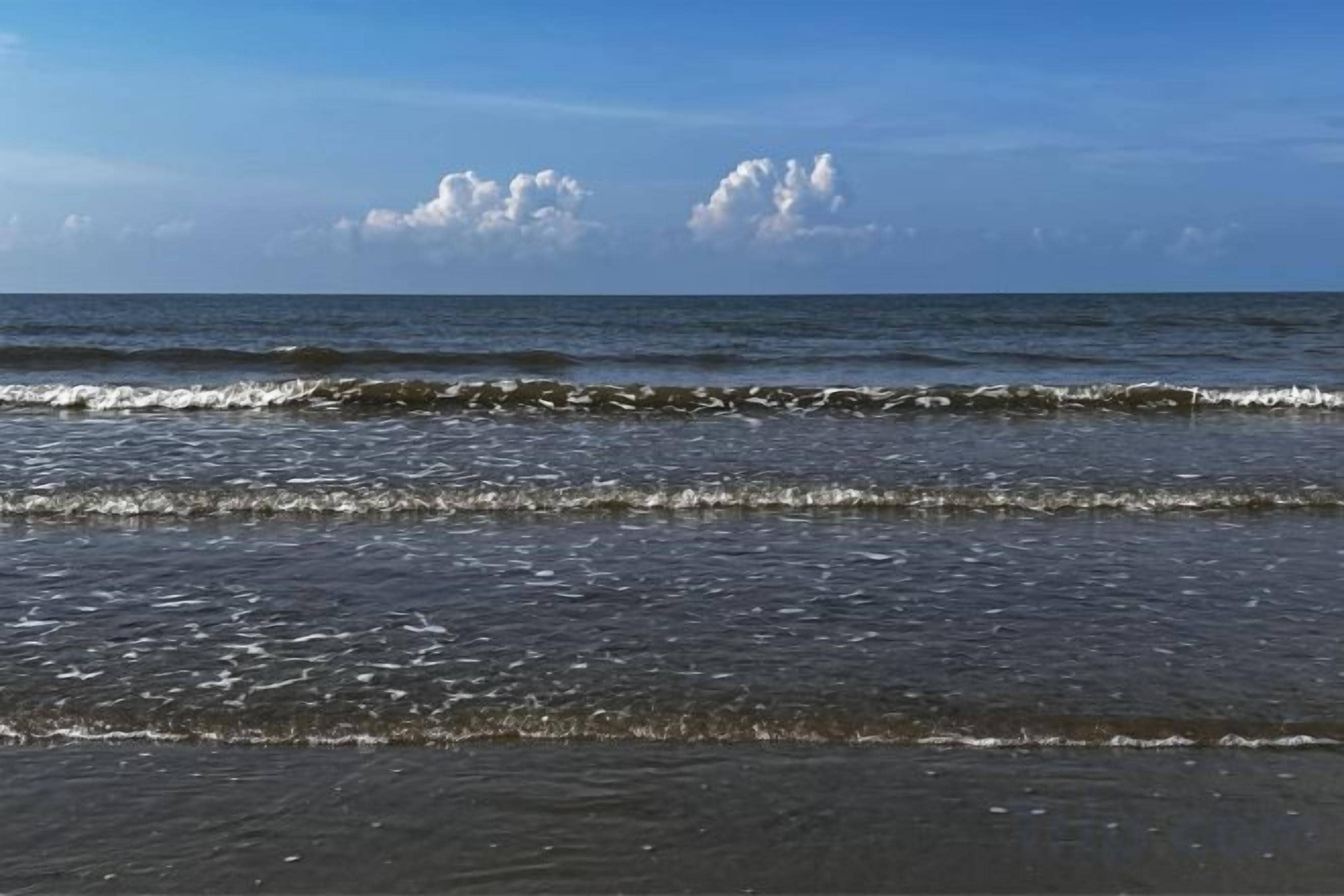 Ein Strand mit Wellen und blauem Himmel.