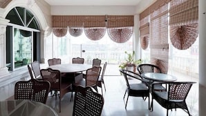 A dining area with a round table and wicker chairs, large windows with decorative blinds, and a view of the city. - Lotto Hotel (Dongxing)
