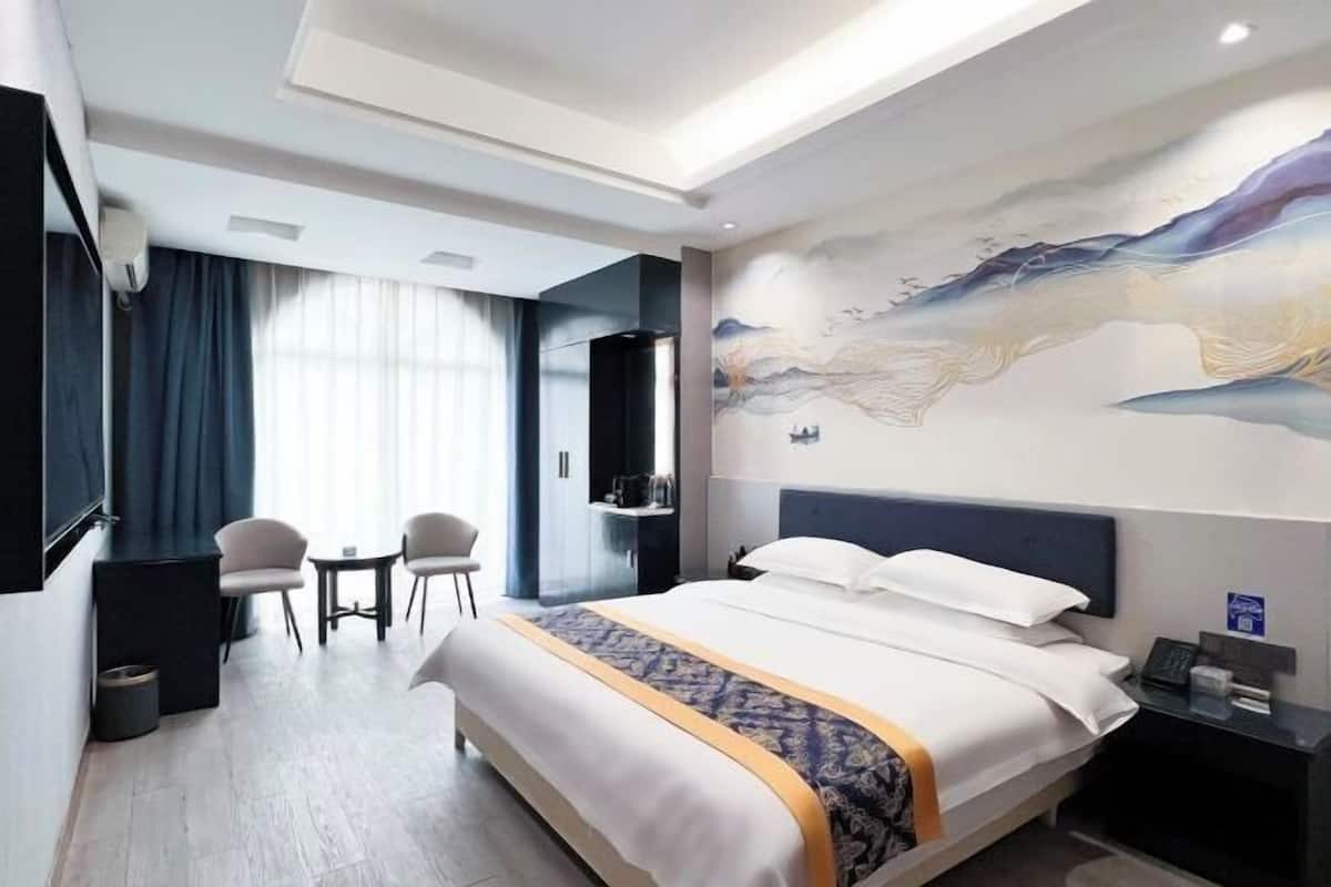 Una habitación de hotel con cama, escritorio, silla, televisor y un mural en la pared.