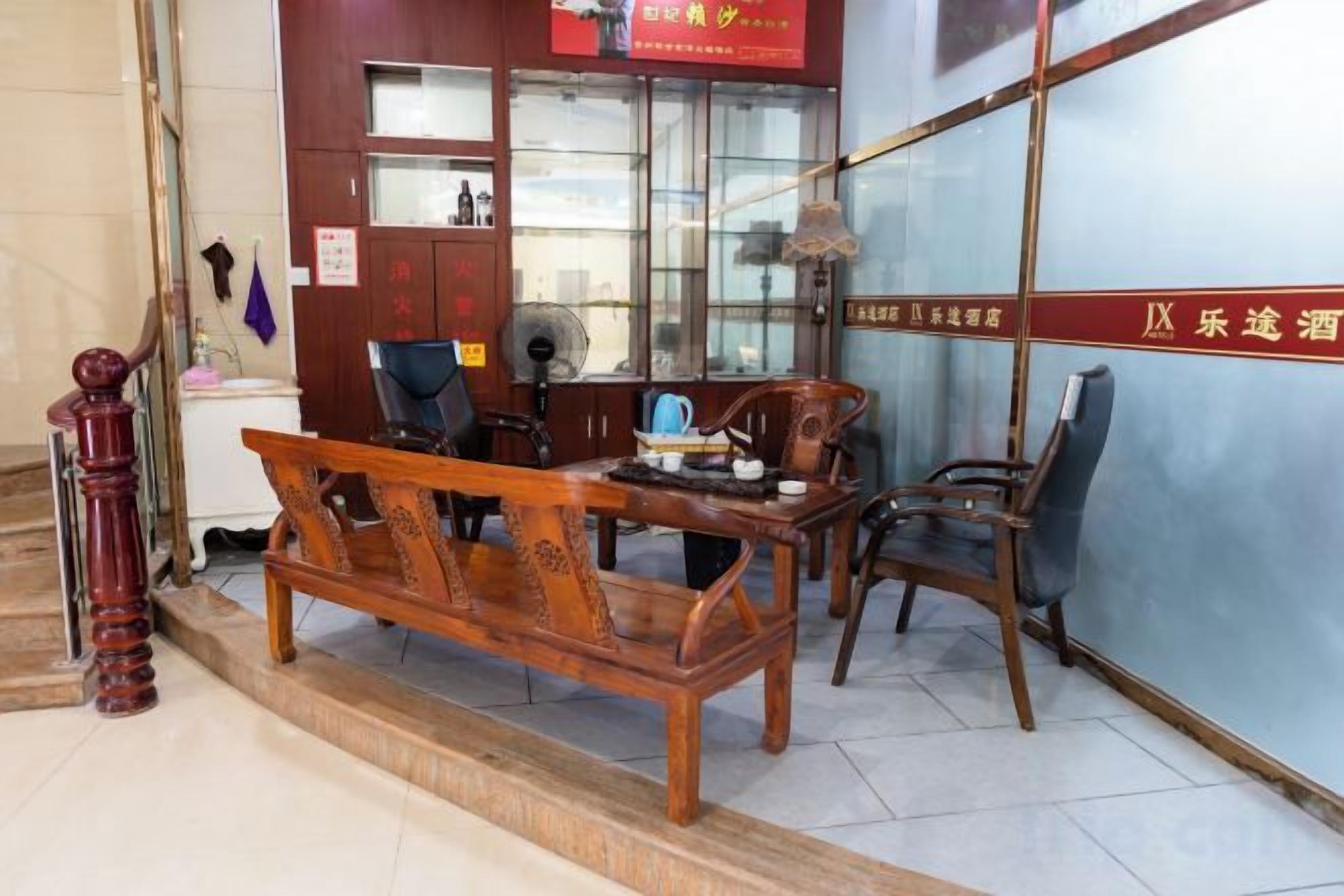 Un sofá y sillones de madera tradicionales en una habitación con suelo de baldosas, un escritorio y un ventilador.