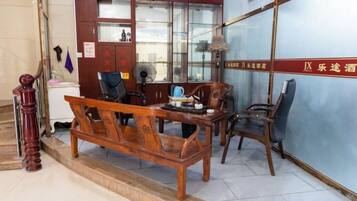 A traditional wooden sofa and chairs in a room with a tiled floor, a desk, and a fan.