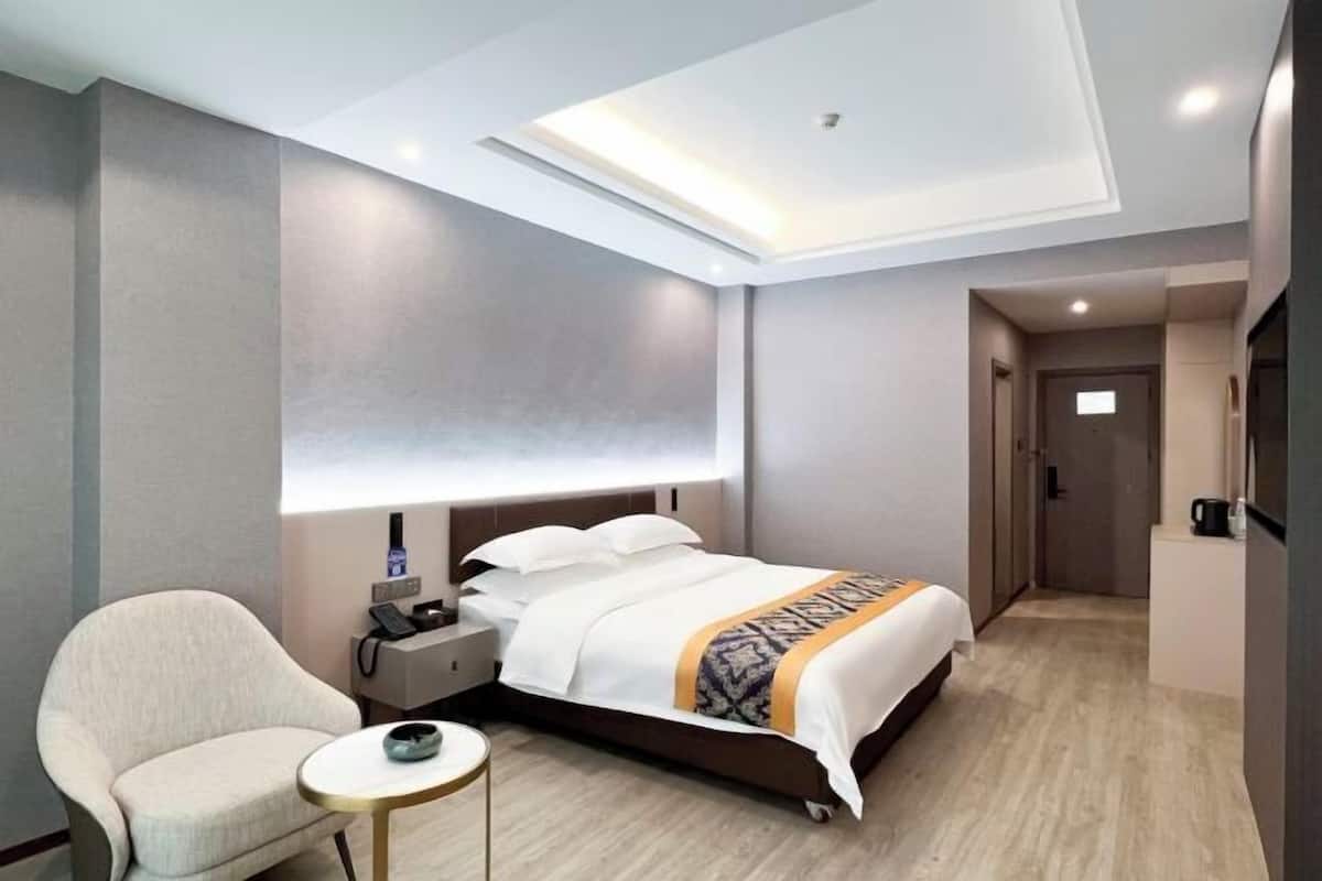 Una habitación de hotel moderna con cama, mesita de noche, lámpara, silla y una pequeña mesa con una taza.
