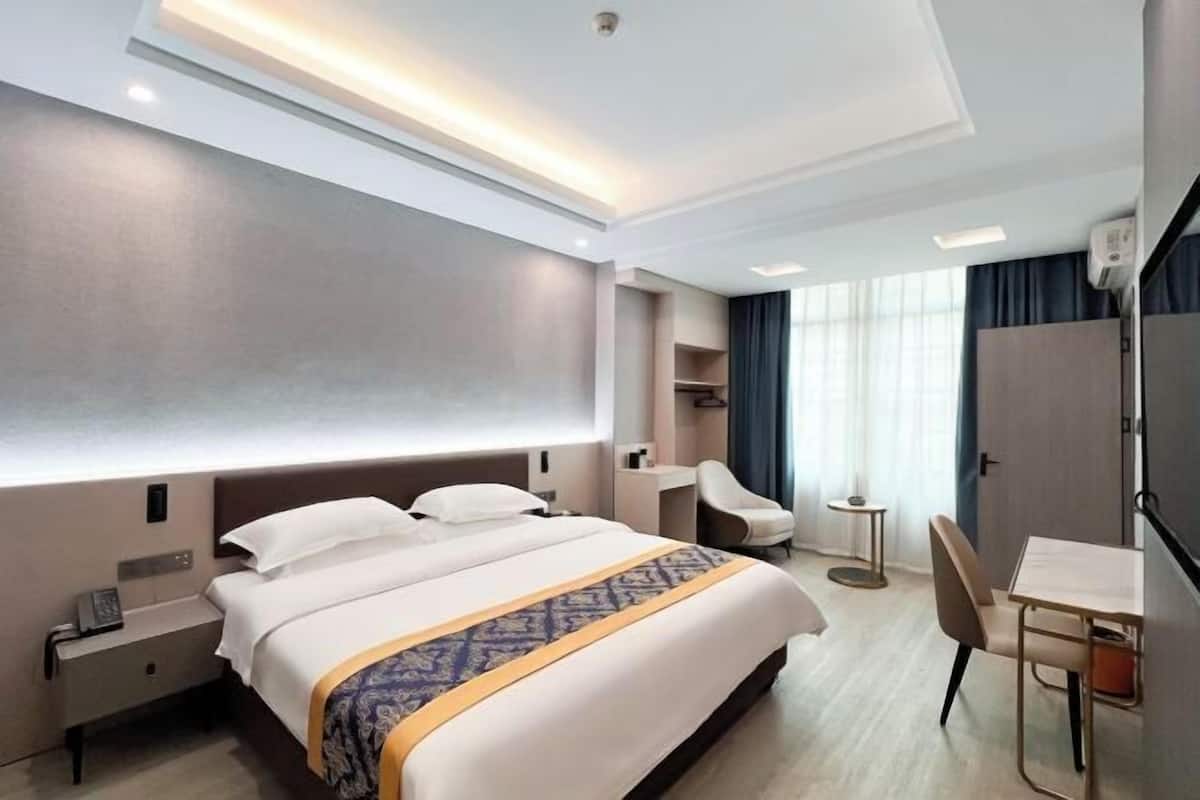 Habitación de hotel con una cama grande, mesitas de noche, un escritorio, una silla, una pequeña mesa redonda y un armario.
