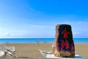 Une scène de plage avec un grand rocher sur lequel figure un texte rouge, un ciel bleu clair et une mer calme.