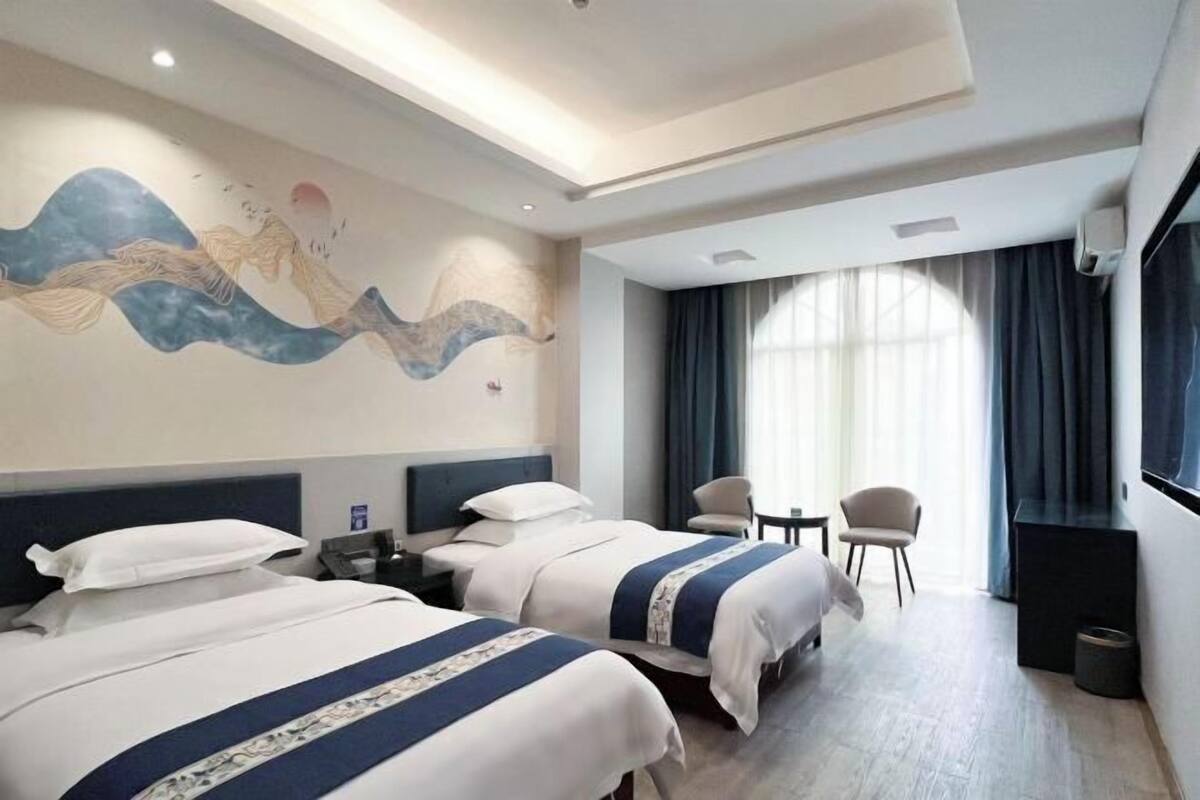 Habitación de hotel con dos camas, un mural en la pared, un televisor, un escritorio y una ventana con cortinas.