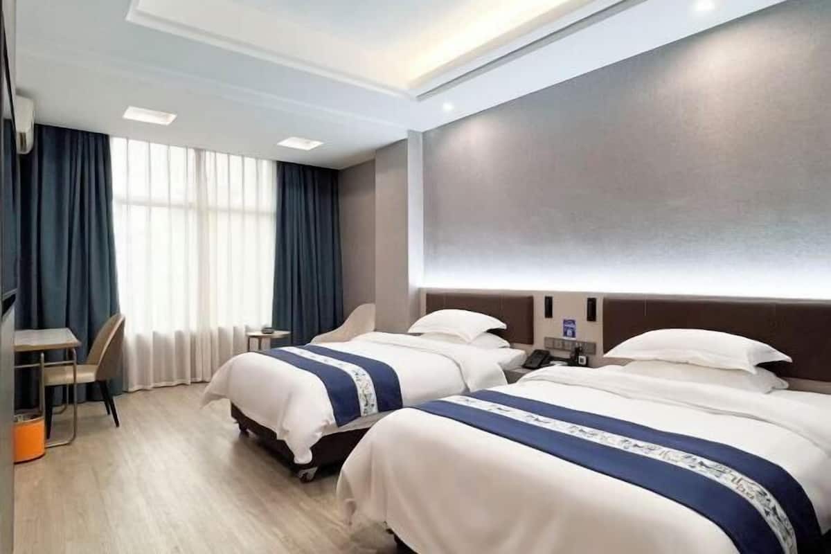 Habitación de hotel con dos camas, un escritorio, una silla, una mesita y un ventanal grande con cortinas.