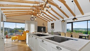 Une cuisine moderne dotée d’un grand îlot central, de poutres en bois au plafond et offrant une vue sur la campagne.