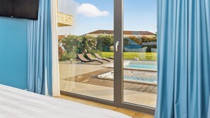 Une chambre avec une porte-fenêtre coulissante donnant sur un espace extérieur comprenant une piscine et des chaises longues.