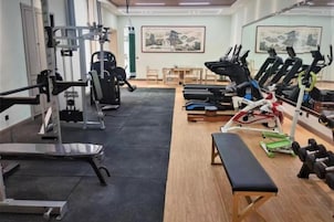 Un gimnasio con máquinas de cardio, equipo de levantamiento de pesas y una banca.