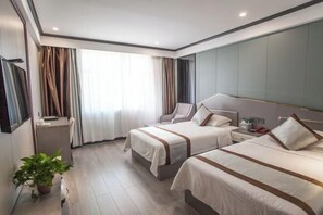 A hotel room with two beds, a desk, a chair, a bedside table, a lamp, and a potted plant.