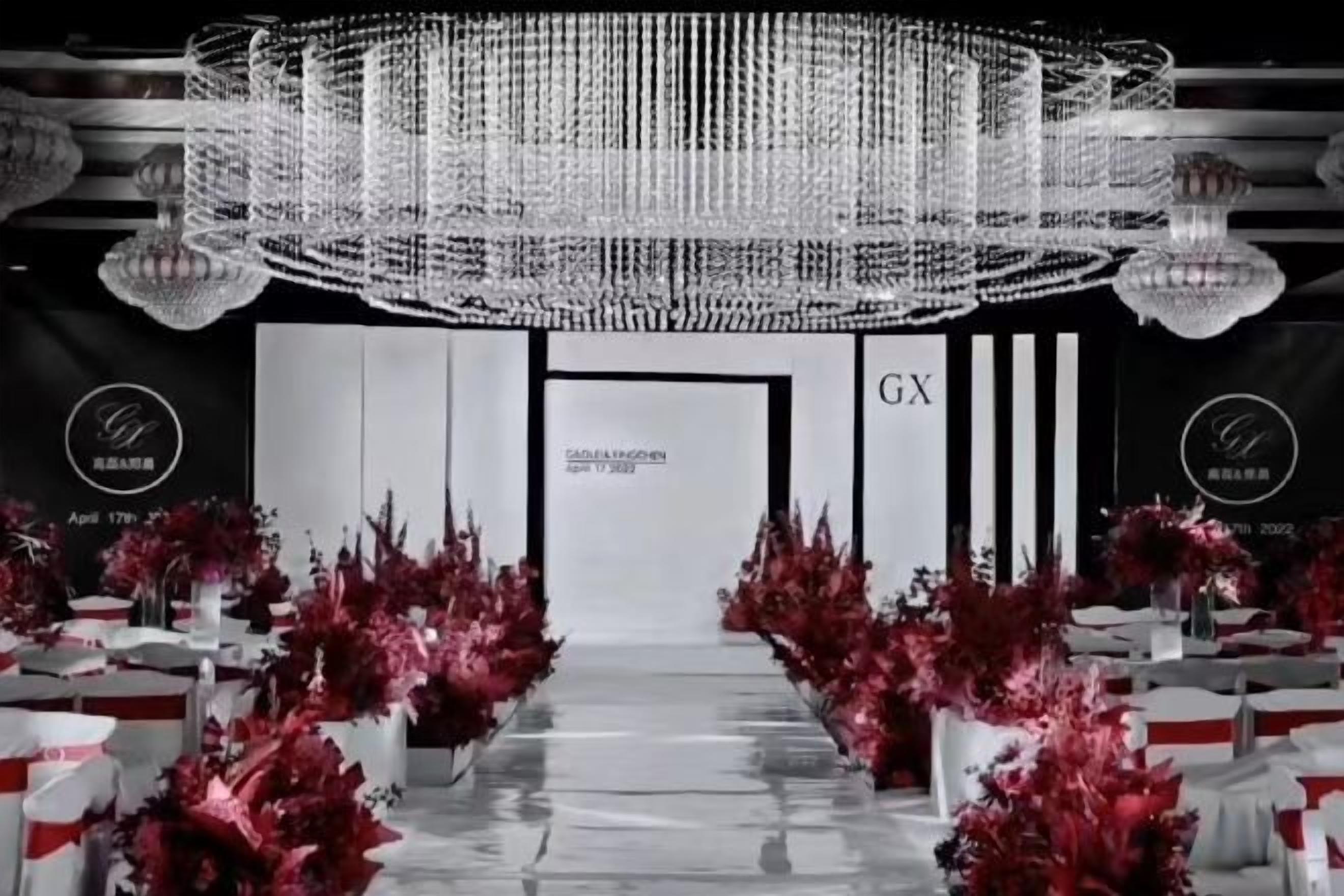 Un salón para eventos elegantes con una araña, arreglos florales rojos y un cartel que dice 'C6X'.
