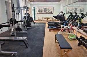 Uma academia com equipamentos de ginástica, um banco e uma mesa com cadeiras.