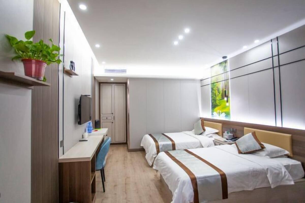 A hotel room with two beds, a desk, a chair, a TV, and a large window with a view.
