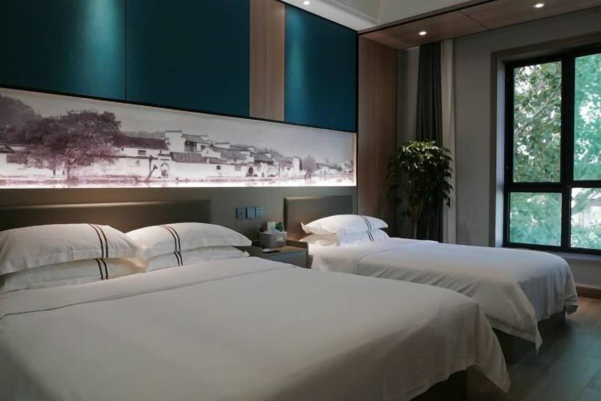 A hotel room with two beds, a large window, and a wall-mounted artwork.