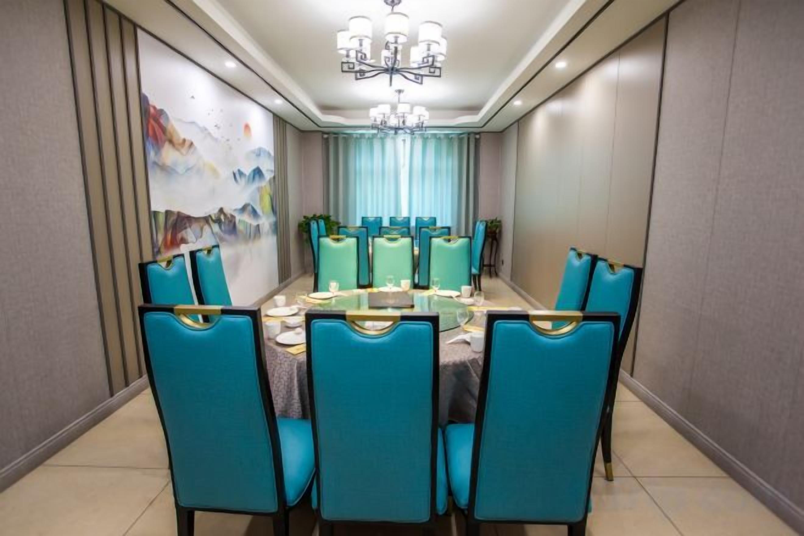 A dining room with a round table, teal chairs, and a chandelier.