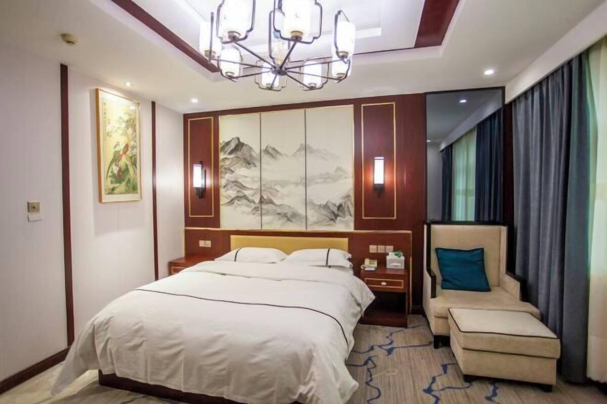 A hotel room with a large bed, a chair, a nightstand, and a wall with artwork.