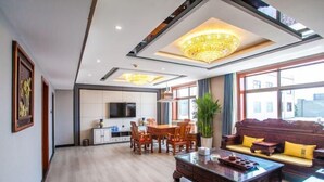 A spacious living area with a wooden floor, a large wooden coffee table, a sofa with cushions, a television, and a dining area with chairs and a table.