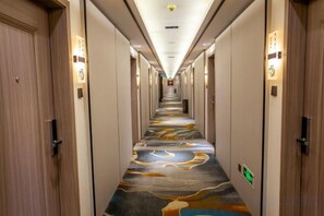 A hotel corridor with doors on both sides, a patterned carpet, and illuminated wall sconces. - Yongping Hotel (Xiong County)