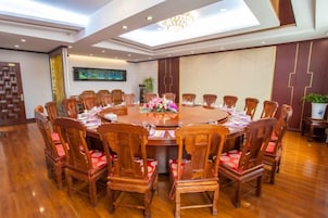 Un salón de conferencias con una mesa redonda, sillas de madera y una araña de cristal.