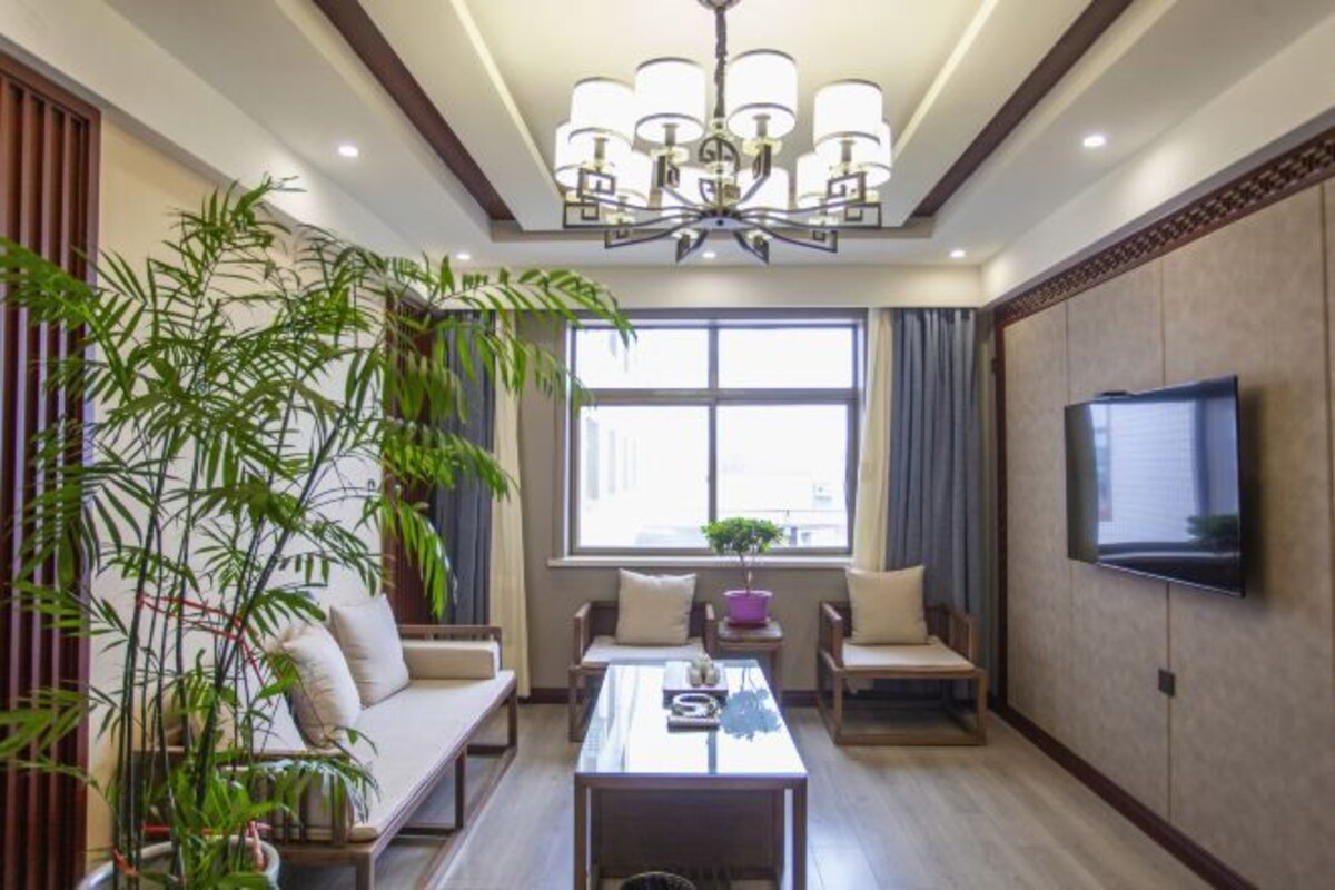 A modern living room with a sofa set, a coffee table, a TV mounted on the wall, and a large window with curtains.