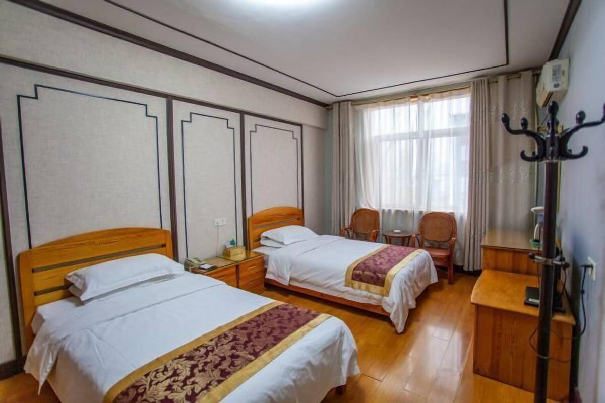 A hotel room with two beds, a desk, a chair, and a coat rack.