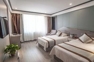 A hotel room with two beds, a desk, a chair, a bedside table, and a potted plant.