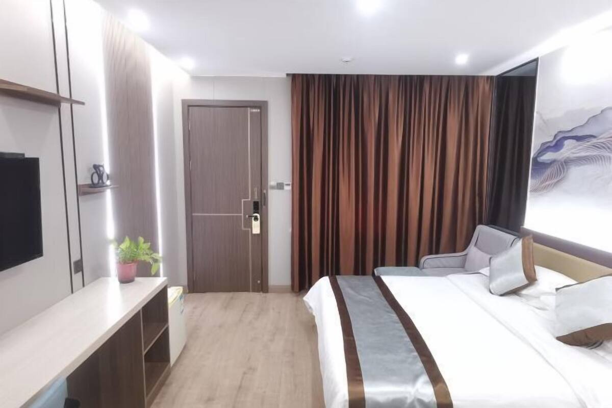 A hotel room with a bed, a desk, a TV, a door, and a curtain.