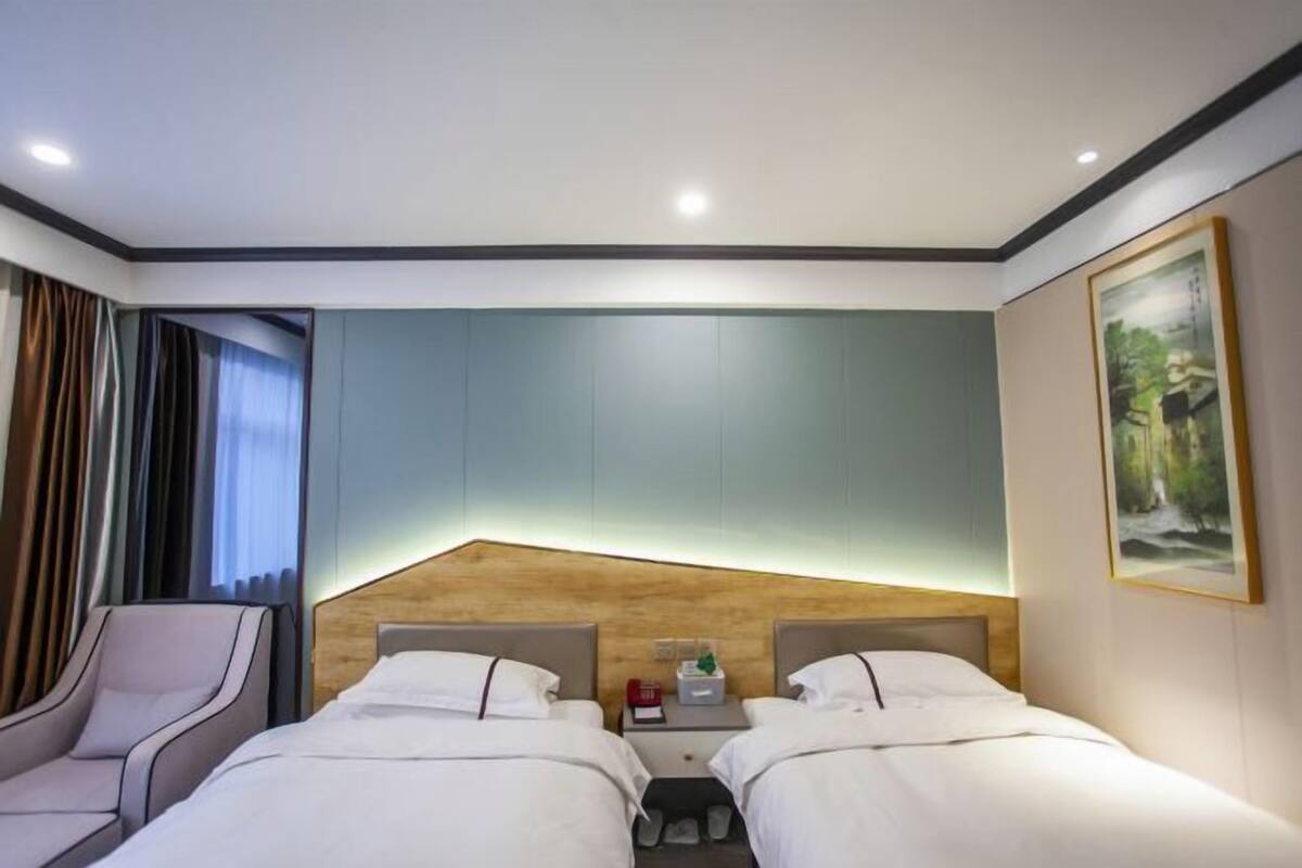 A hotel room with two beds, a nightstand, a chair, and a painting on the wall.
