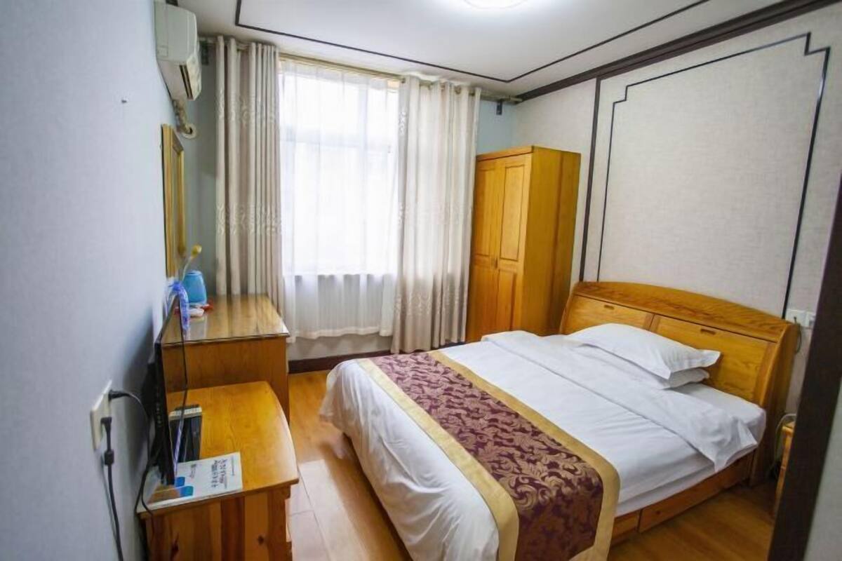 A hotel room with a bed, a wooden wardrobe, a desk with a mirror, and a window with curtains.